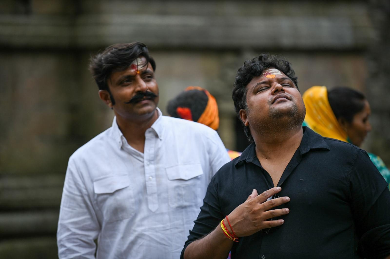 Two yatris at Jageshwar Dham, one with his hand on his heart and eyes closed.