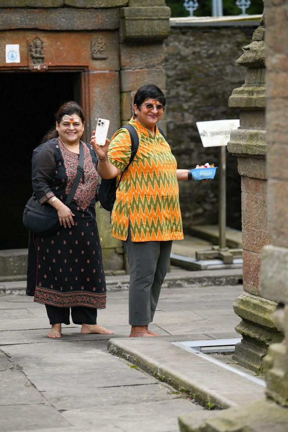 Two yatris waving and smiling in the temple courtyard.